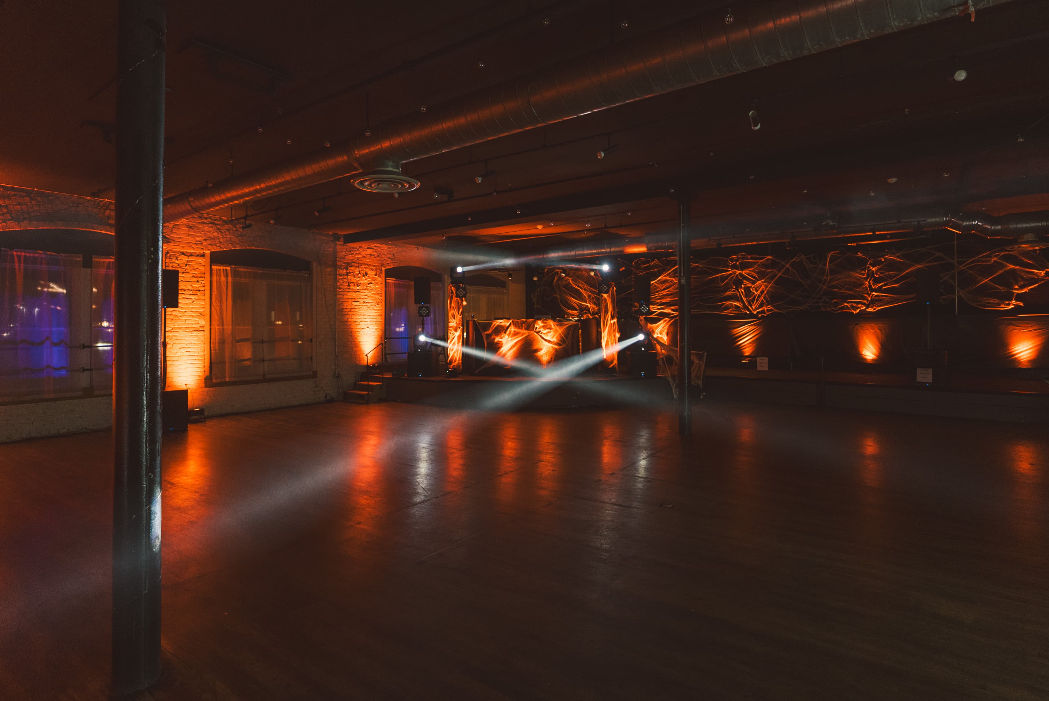 An empty dance floor lit in orange, with cobwebs draped over the DJ booth
