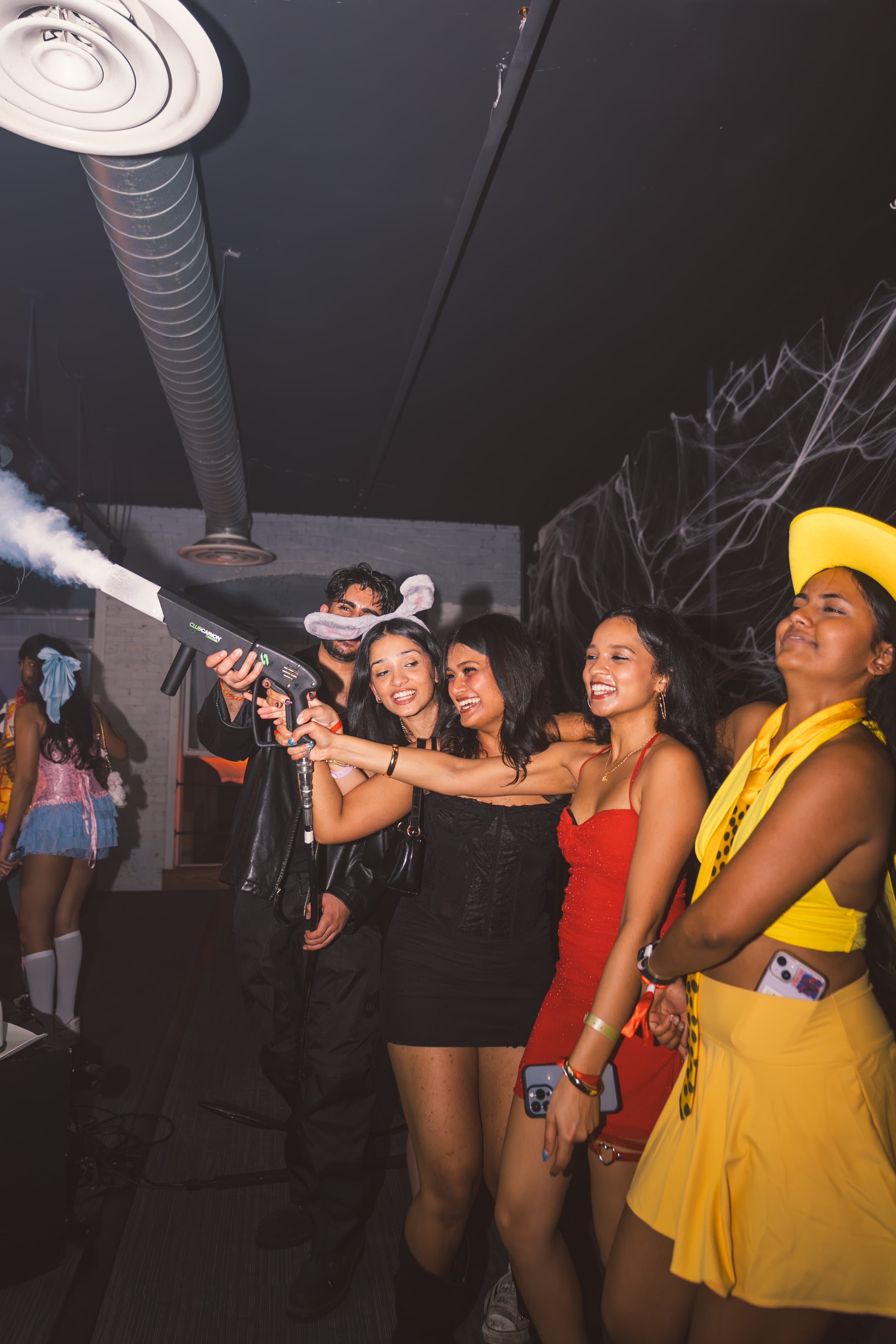 Friends in bright costumes laughing around a fog cannon