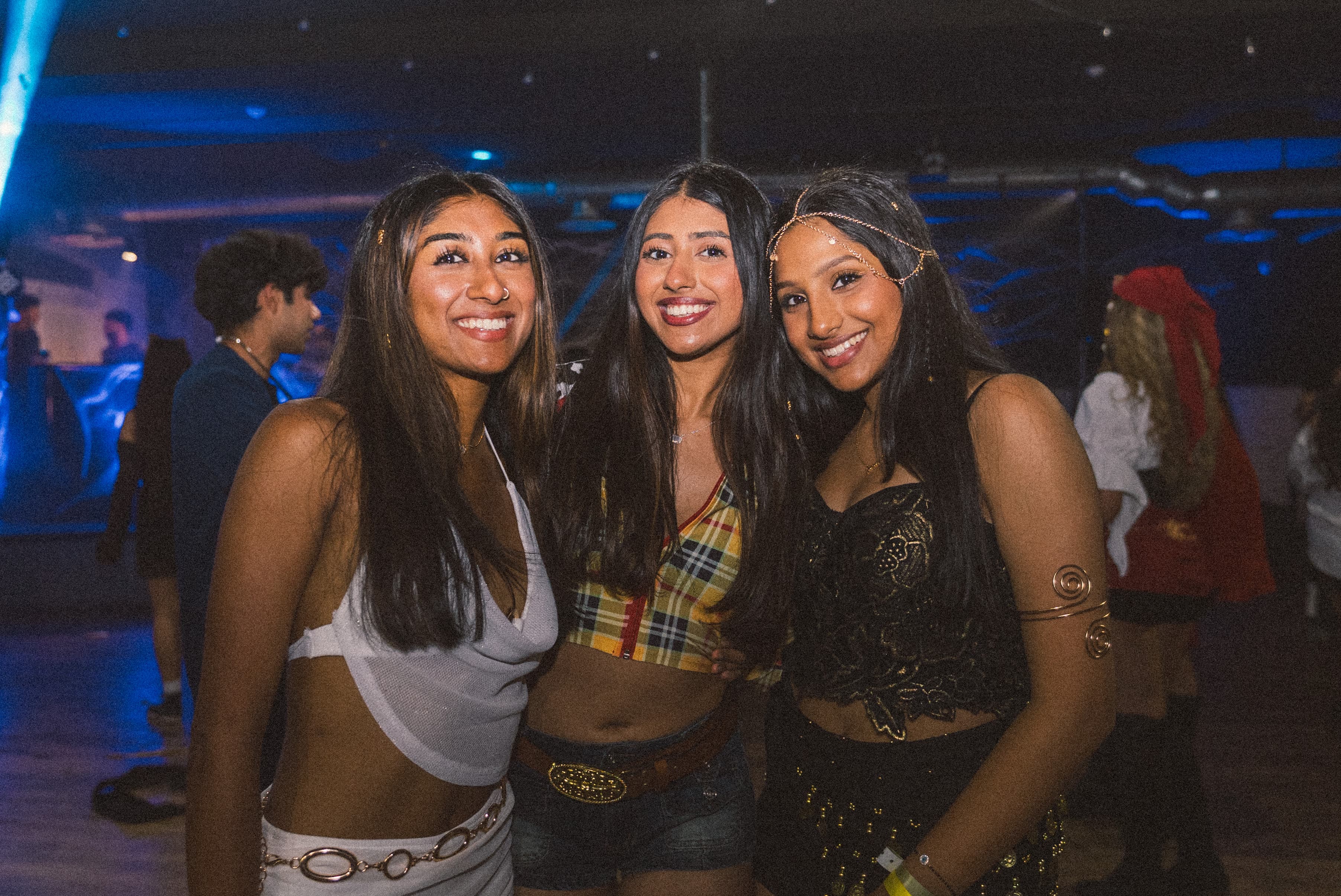 Three friends smiling in costumes under blue lights