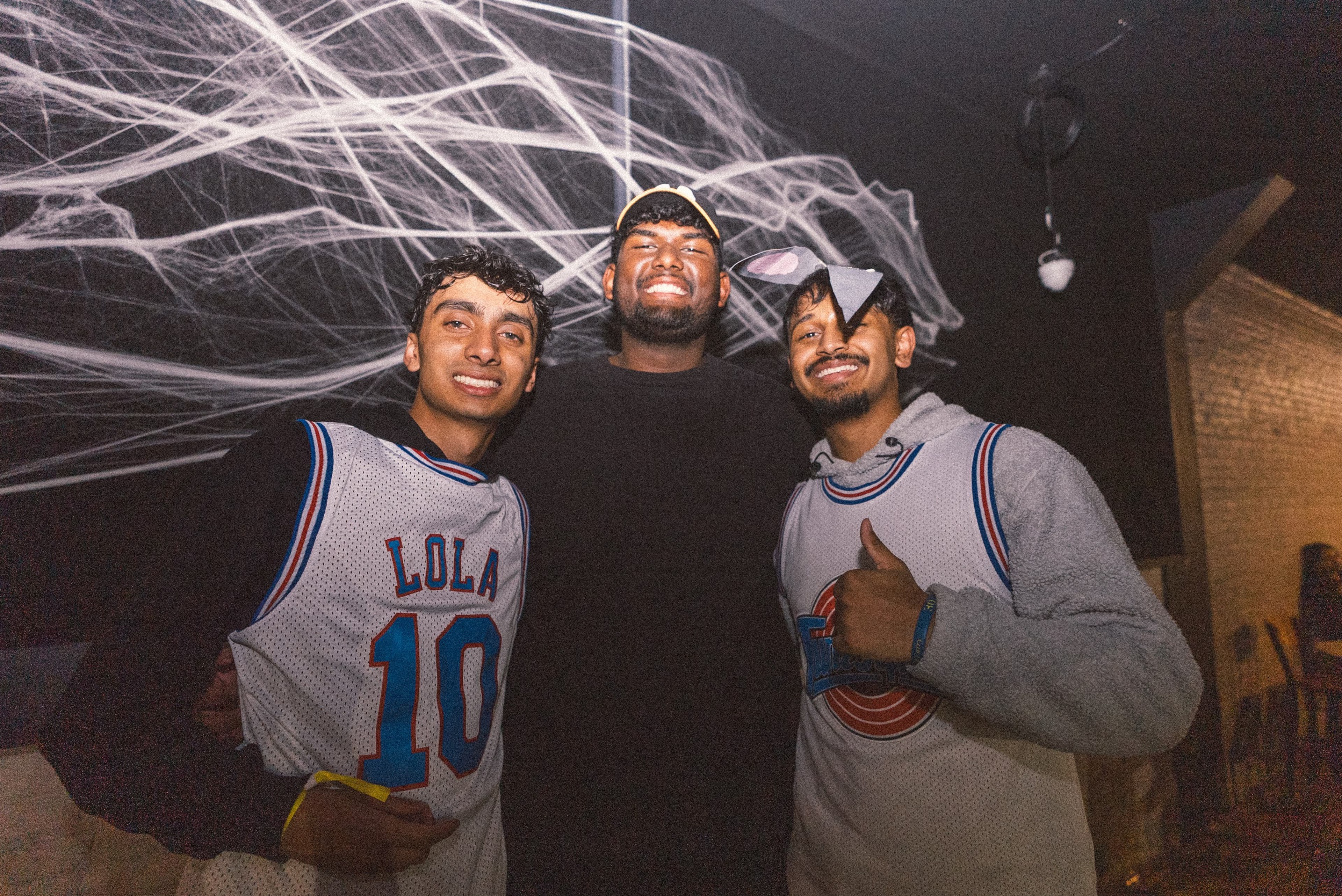 Three friends in basketball jerseys posing in front of a wall of cobwebs