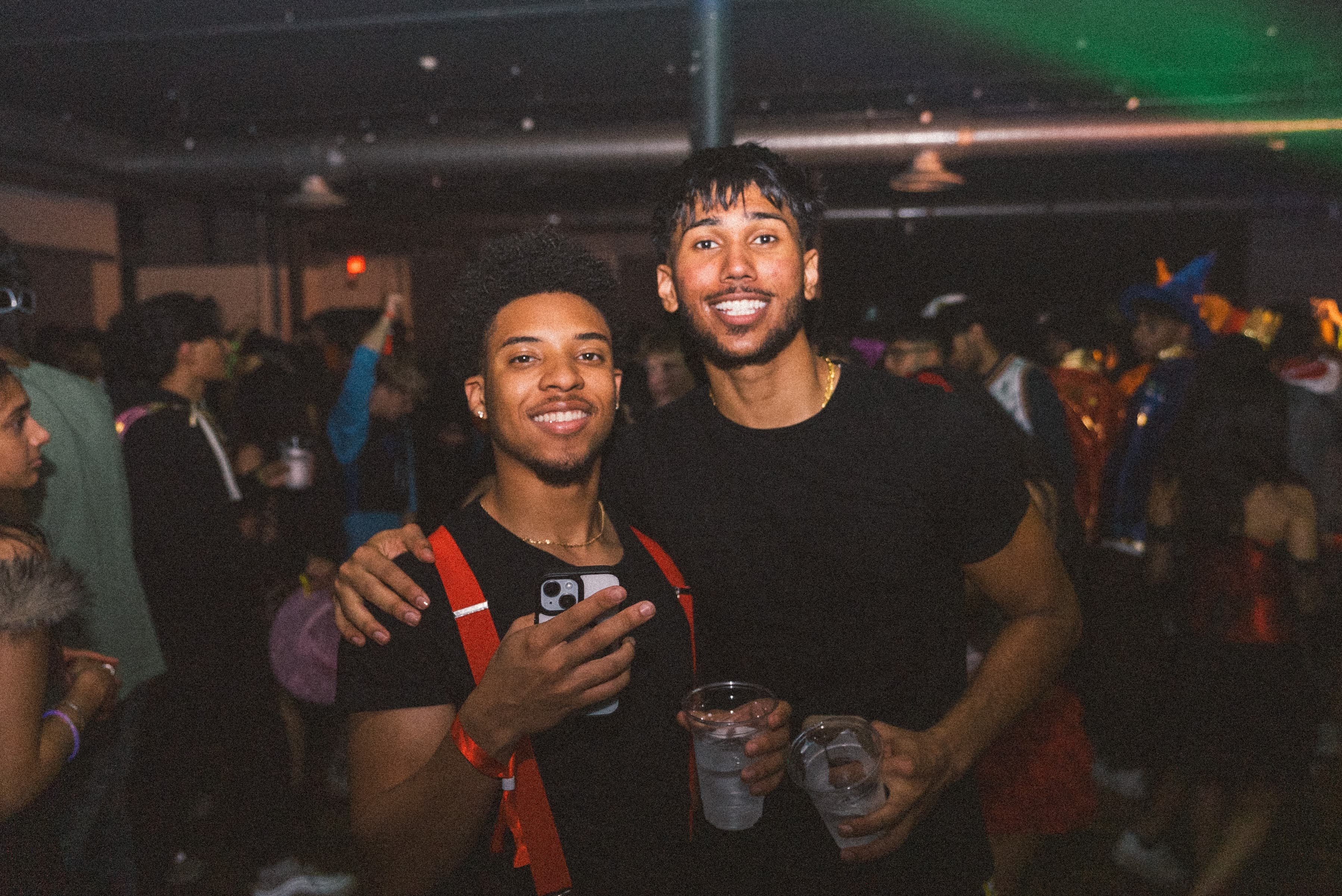 Two friends smiling with drinks on a crowded dance floor